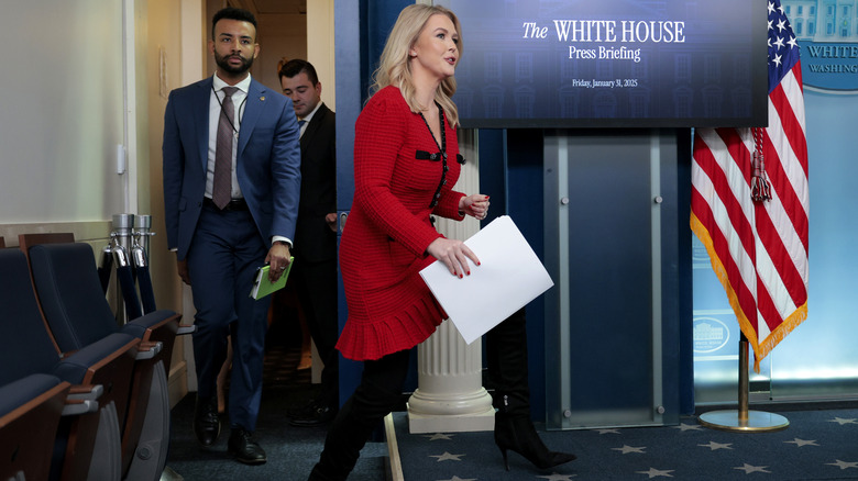 Karoline Leavitt in red sweater dress stepping onto White House platform