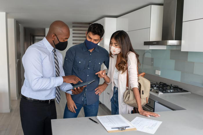 Two people conferring with another person in the kitchen of a home.