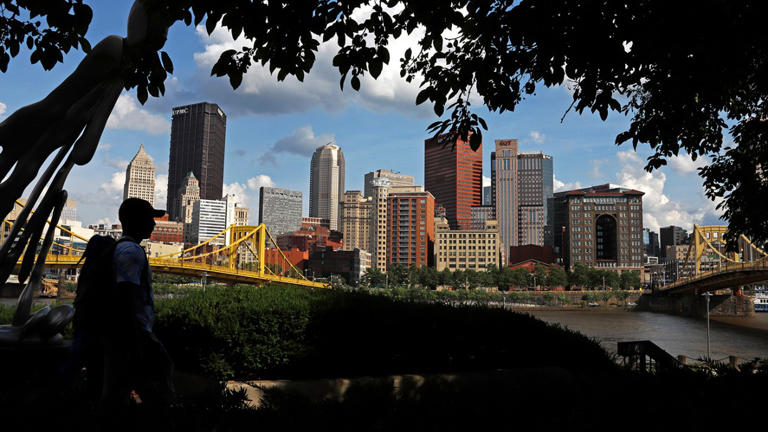 The skyline of Pittsburgh is framed by couple walking through a park on the Northside on Wednesday, June 26, 2019. (AP Photo/Gene J. Puskar)