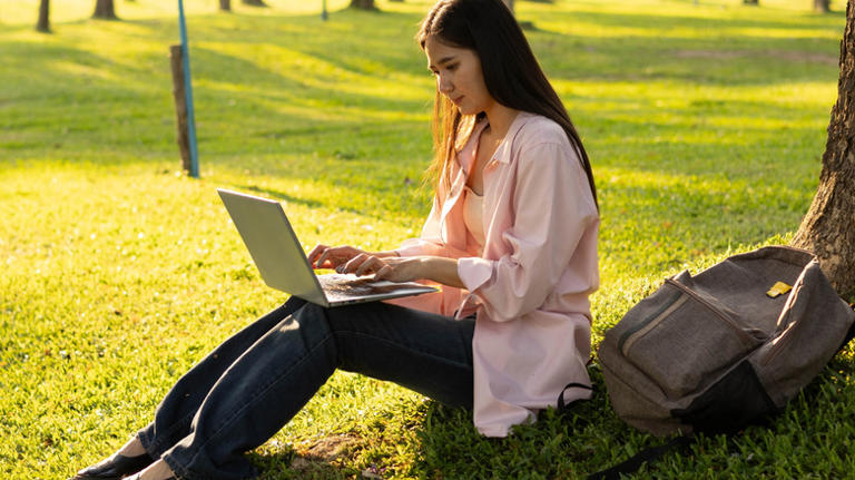 Woman slouching while using laptop on lap outdoors