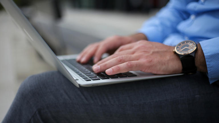 Man using laptop on lap while in business clothes