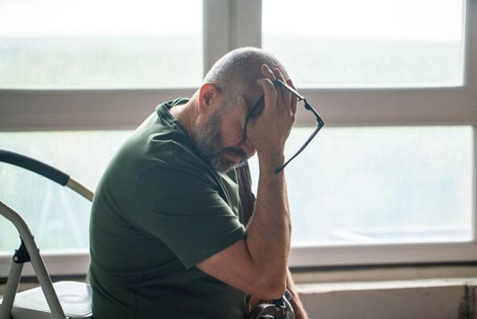 Exhausted Senior Man Sitting with Glasses in Hand by Window