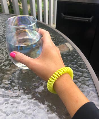 Hand with a neon coiled bracelet holds a glass of water on a patio table