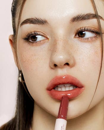 Person applying lipstick while looking away, showcasing a glossy finish