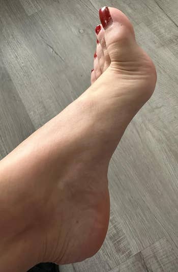 Close-up of a person's foot with red nail polish, resting on a wood floor
