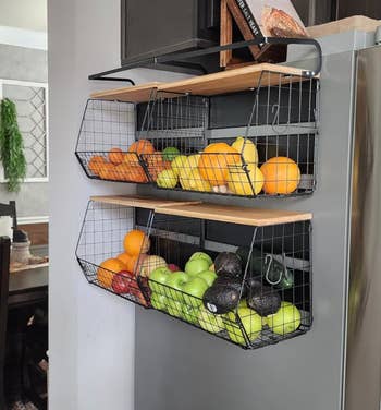 Wire baskets mounted on a kitchen wall hold various fruits, including oranges, lemons, apples, and avocados, showcasing organized storage solutions
