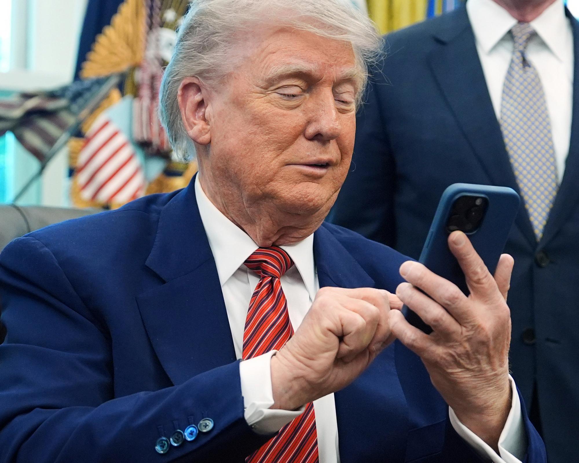 Donald Trump silences his mobile phone, which rang twice as he was speaking to reporters, in the Oval Office of the White House on 23 May 2025. Photograph: Evan Vucci/AP