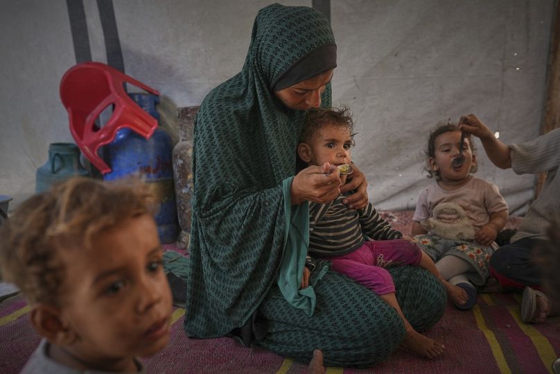 Una mujer palestina alimenta a sus hijos en una tienda de campaña que alberga a una familia desplazada en el centro de la ciudad de Gaza, el sábado 24 de mayo de 2025. Jehad Alshrafi/Copyright 2025 The AP. All rights reserved