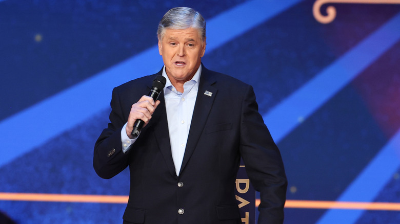 Sean Hannity speaking onstage at an event in a suit