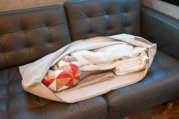 Bedding organizer bag on a leather sofa holding folded blankets and quilts. Ideal for home storage solutions