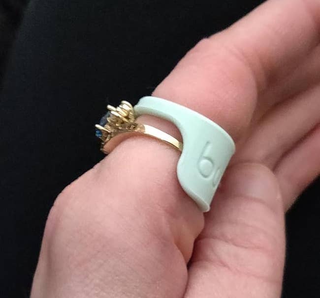 Hand wearing a gold ring with a diamond design, supported by a silicone ring adjuster for better fit