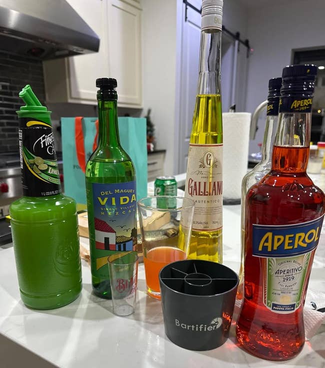 A variety of colorful spirits and liquor bottles displayed on a kitchen counter, with bar accessories in the foreground