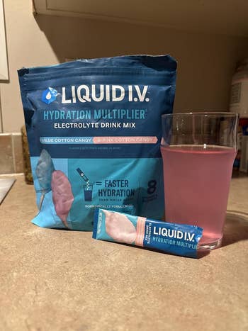 Liquid I.V. Hydration Multiplier electrolyte drink mix in blue bag with glass of pink beverage and single serving packet in front