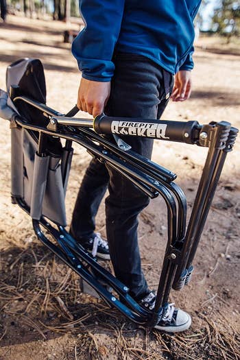 person carrying the folded up fire pit chair by its handle