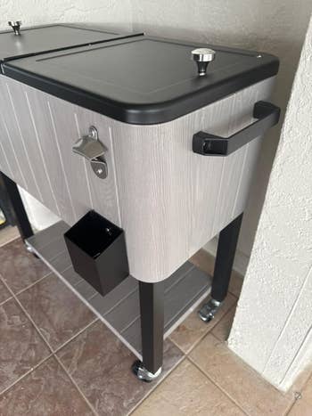 Portable cooler on wheels with a bottle opener, attached compartment, and handles