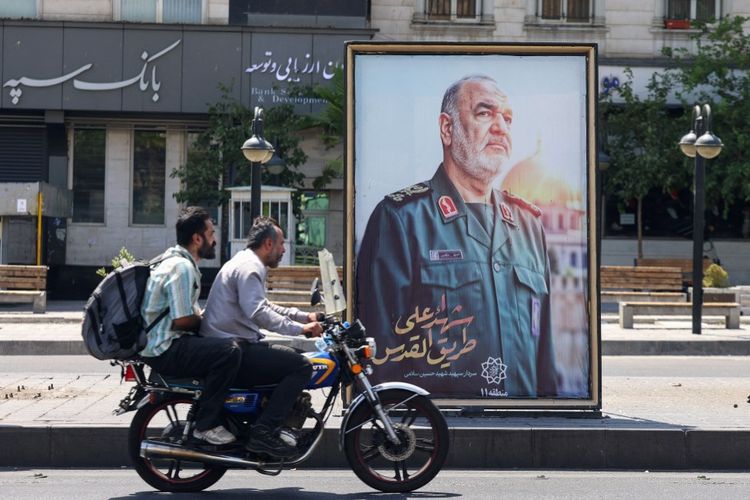 Warga Iran mulai mengungsi dengan kendaraannya di samping poster komandan Korps Garda Revolusi Islam (IRGC) Iran yang terbunuh, Hossein Salami, yang tewas setelah serangan Israel terhadap sejumlah target di Iran, dipasang di sebuah alun-alun Teheran pada 16 Juni 2025.