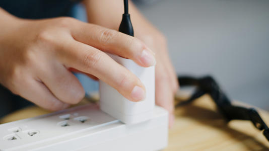 A person plugging in phone charger to extension cord