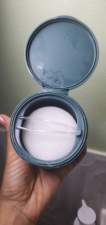 Open container with cotton pads and tweezers, held by a hand