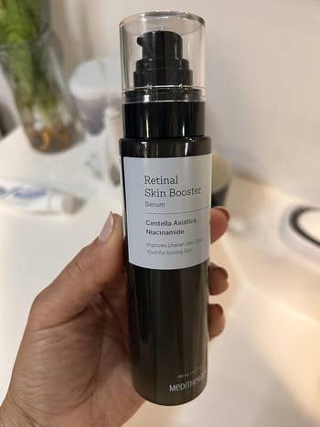 A hand holds a bottle of Meditherapy Retinal Skin Booster Serum, labeled for improving uneven skin tone and achieving youthful-looking skin