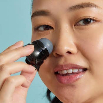 Person smiling while applying a skincare roller to their face, showcasing a beauty product in use