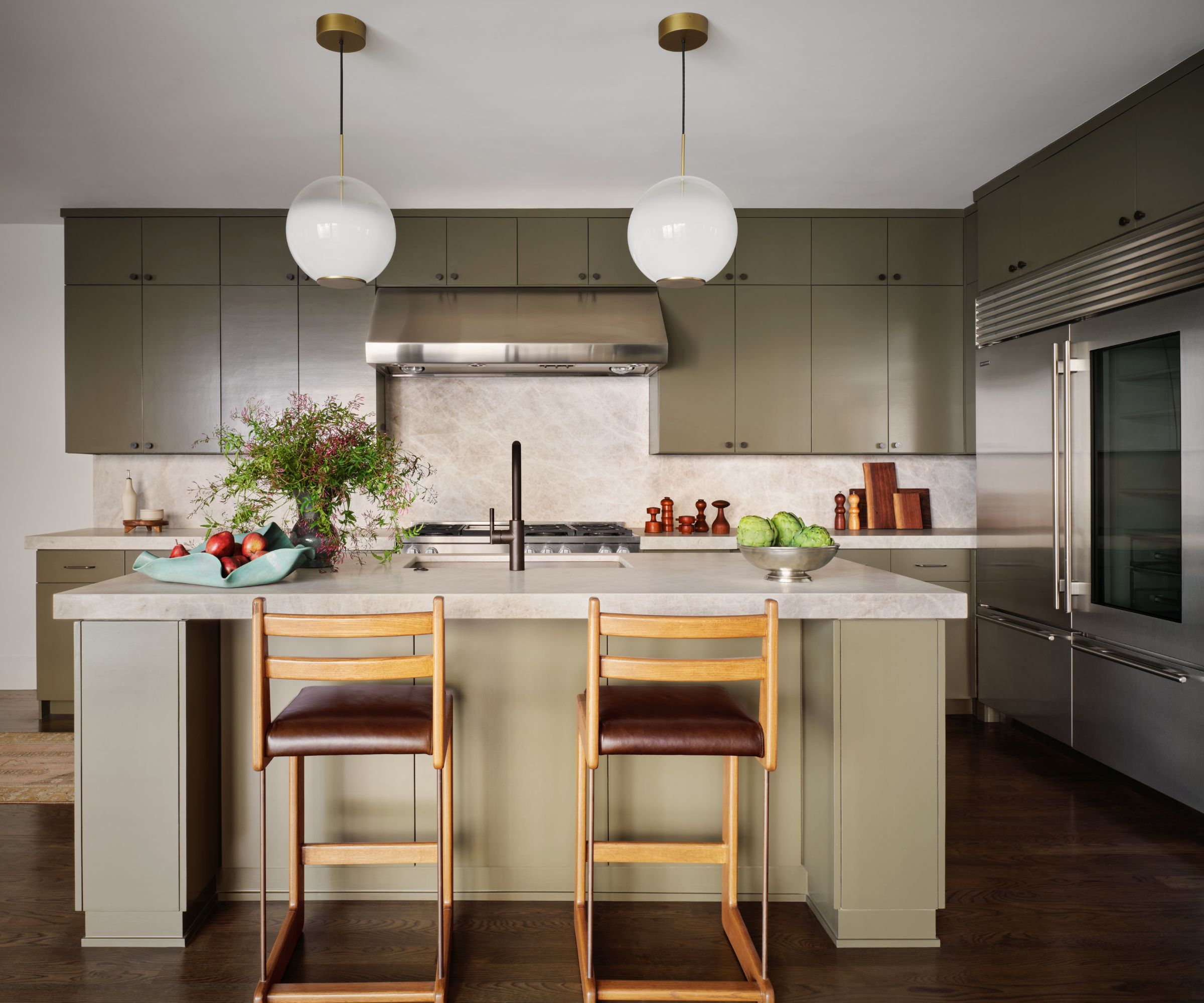 Modern kitchen with sage green cabinets, marble sage green island, wood bar stools and two round pendant lights
