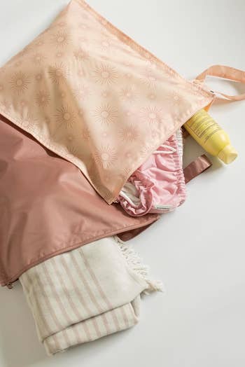 Reusable bag with sun pattern, holding a yellow tube and folded pink-striped towel. A hint of fabric peeks out, suitable for shopping context