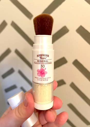 Person holds Hawaiian Tropic Mineral Translucent Sunscreen Powder SPF 30 with a built-in brush in original packaging