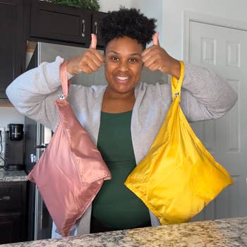 Person smiles, giving thumbs up while holding reusable shopping bags in a kitchen setting