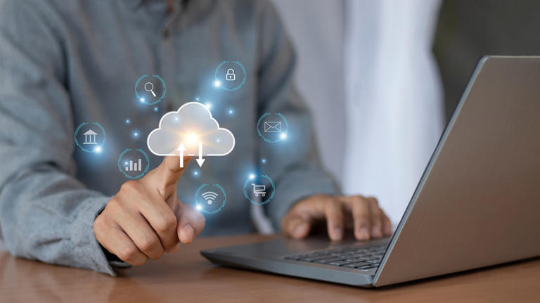 A person using a laptop and touching an imaginary cloud icon
