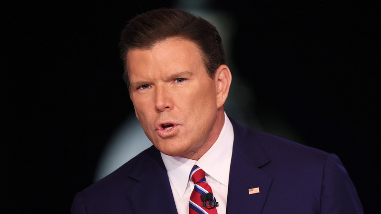 Bret Baier speaking while sitting down wearing a suit and striped tie