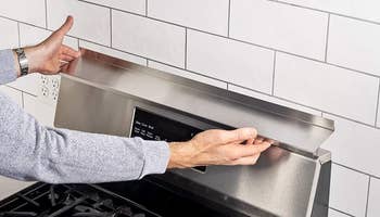 person putting a stainless steel stove shelf on top of a stove