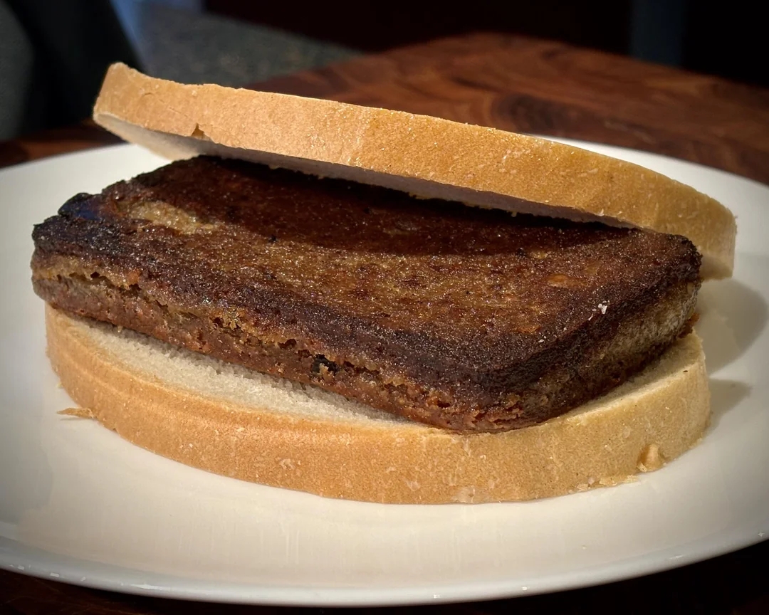 A cooked rectangular steak is sandwiched between two slices of white bread on a plate