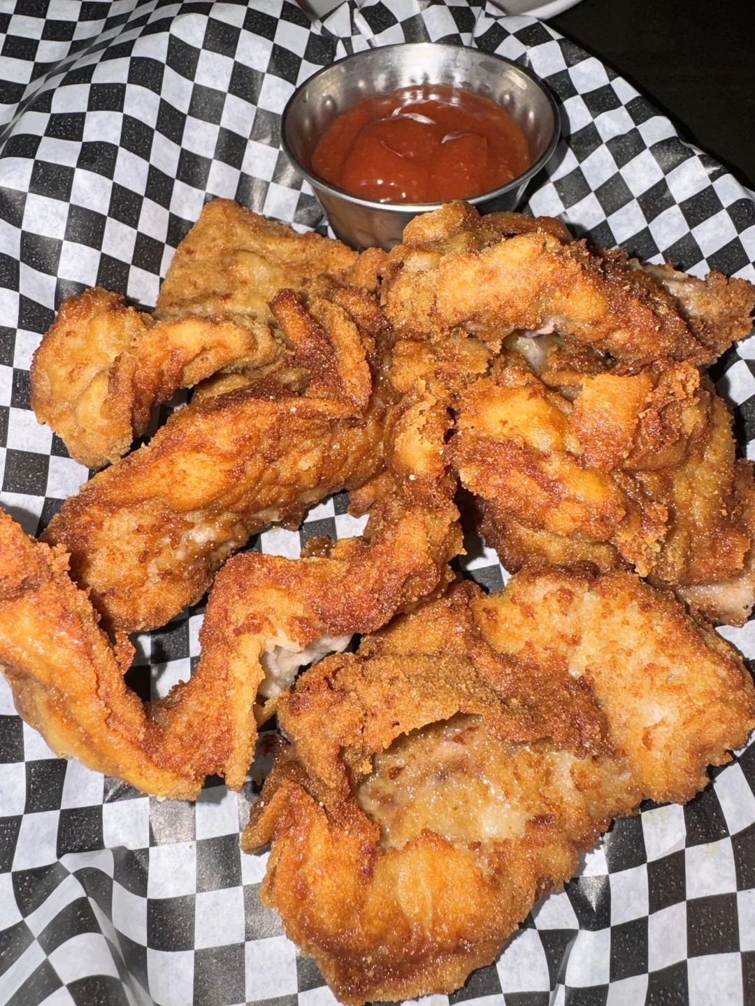 Plate of crispy fried mushrooms with a small dish of dipping sauce on a checkered paper background