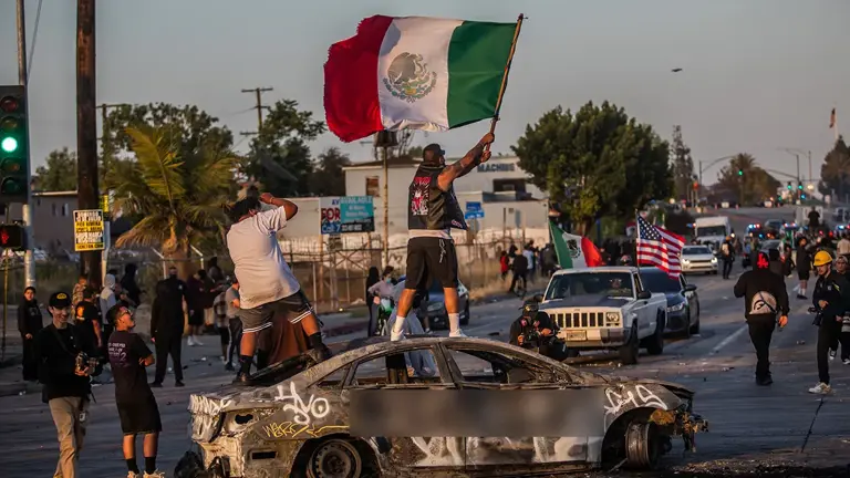 A protester stands on a burned car holding a Mexican flag on Atlantic Ave. on June 7, 2025 in Paramount, California. Getty Images