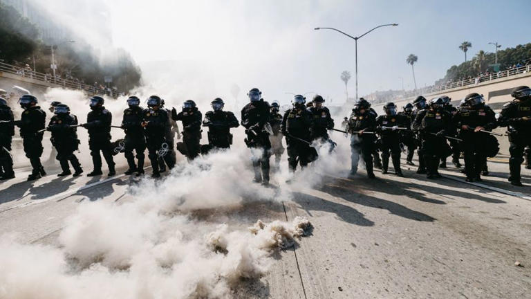 El humo llena el aire mientras agentes del orden con equipo antidisturbios avanzan durante las protestas en Los Ángeles el domingo. - David Pashaee/Middle East Images/AFP/Getty Images
