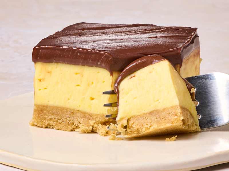 Layered dessert with a creamy yellow filling, chocolate ganache topping, and a crumbly base on a plate.