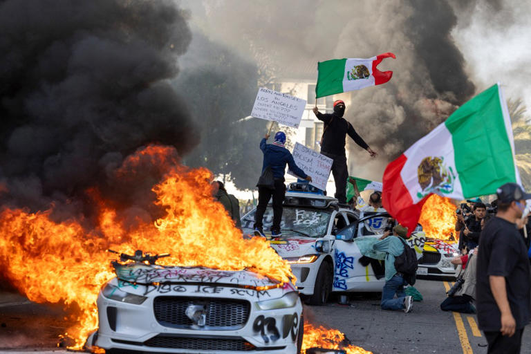 Demonstrators wave flags from atop a wrecked car in LA. AFP via Getty Images
