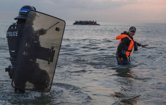 A French policeman enters the sea to try and stop migrants boarding small boats