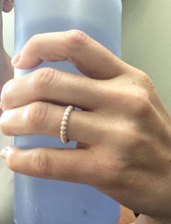 Hand holding a large bottle, wearing a simple beaded ring, suggesting hydration as part of a shopping lifestyle choice