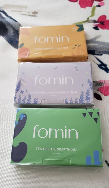 Three packages of Fomin soap thins in sweet orange, lavender, and tea tree oil scents, displayed on a floral background
