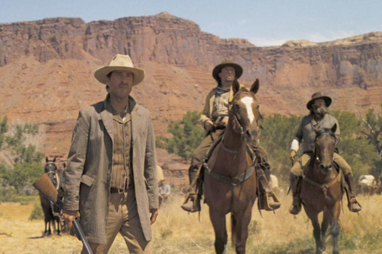 One man stands as two others ride on horses