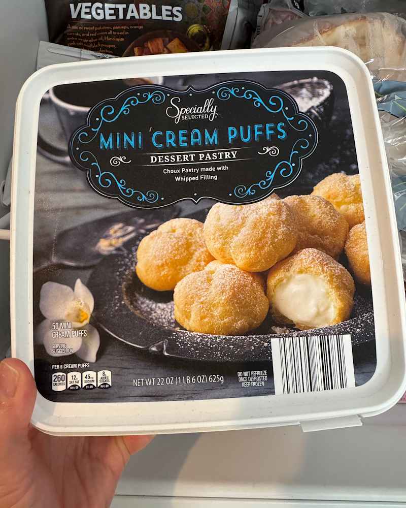 Someone holding up a container of frozen Specially Selected Mini Cream Puffs at Aldi