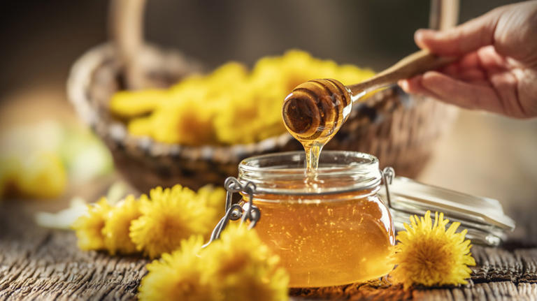 Hand holds dipper over honey pot with flowers
