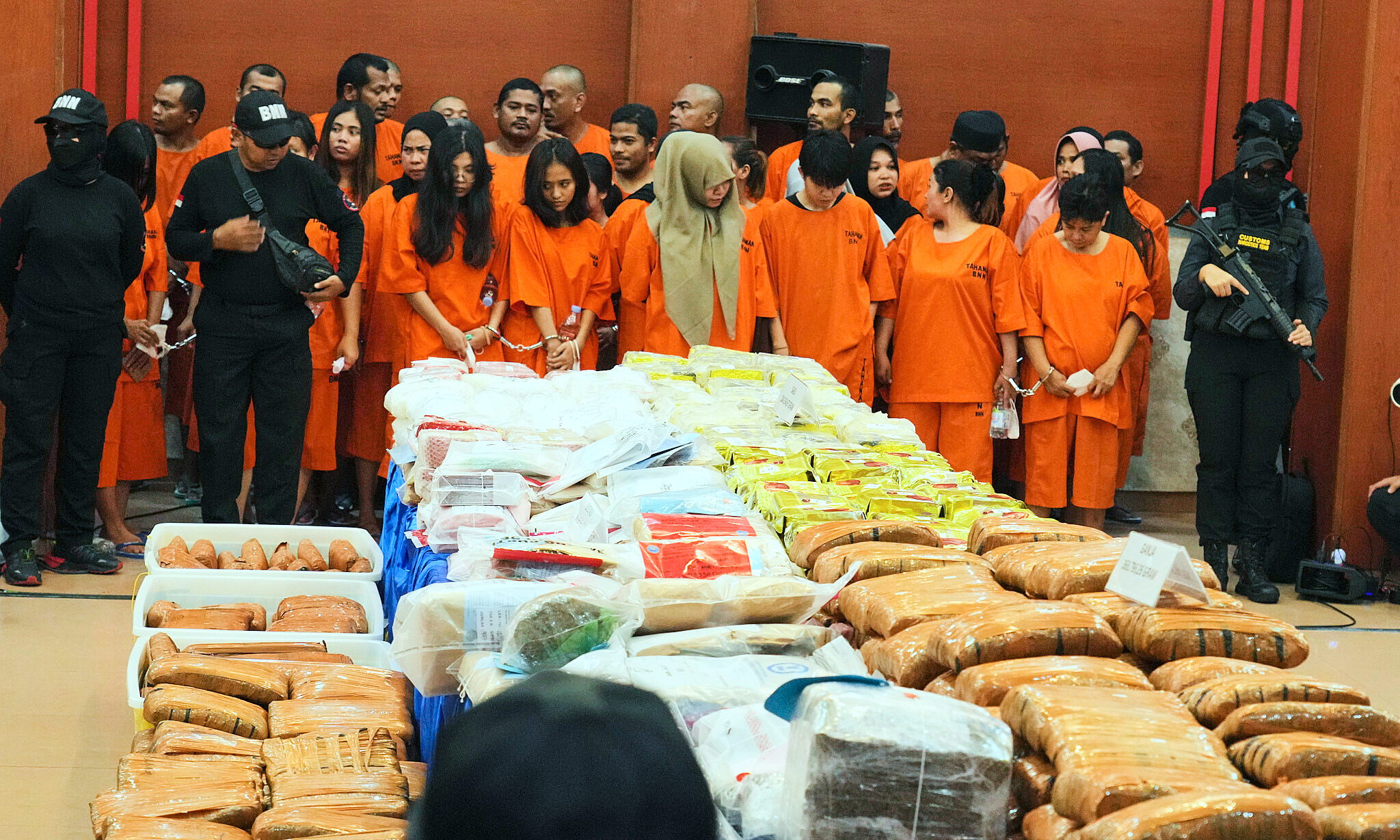 Индонезийские полицейские стоят на страже рядом с подозреваемыми и различными наркотиками, изъятыми в ходе общенациональных репрессий за последние несколько месяцев, перед началом пресс-конференции в штаб-квартире индонезийской таможни в Джакарте, Индонезия, 23 июня 2025 года. Фото AP