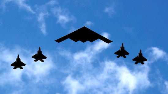 A U.S. Air Force B-2 Spirit Stealth Bomber (C) is flanked by 4 U.S. Marine Corps F-35 fighters