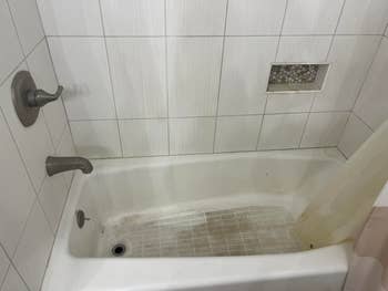 Bathroom with a tiled shower and bathtub featuring a built-in shelf and faucet. The tub appears used, and water stains are visible