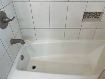 A white bathtub with a textured tile wall, chrome fixtures, and a small inset shelf