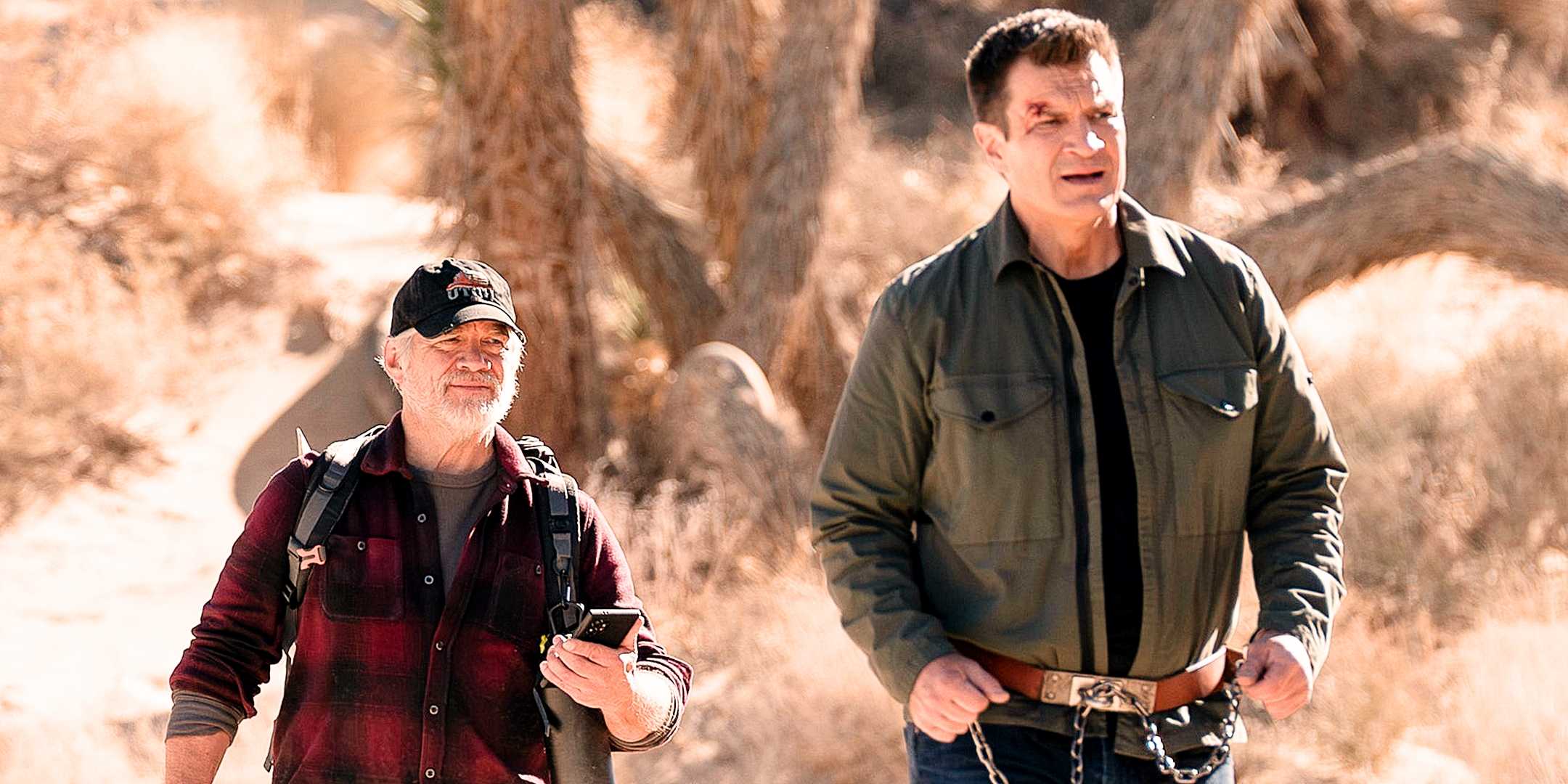 Oscar Hutchinson, in plaid and a black hat, points a gun at John Nolan, in a Green coat and chains, in the desert from The Rookie