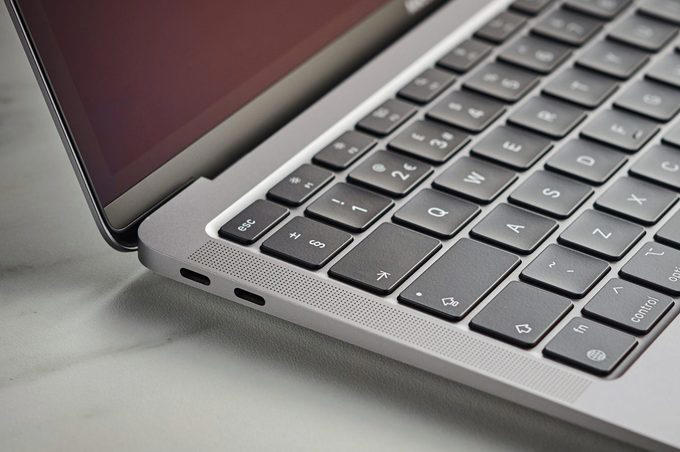 Laptop keyboard sits partially open, revealing keys and ports, on a smooth, light-colored surface.