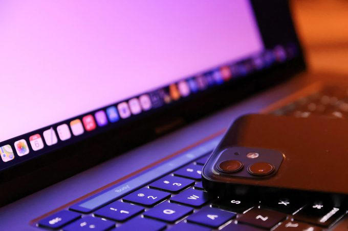 A smartphone rests on a laptop keyboard, with the laptop's screen displaying colorful app icons on a pink background.